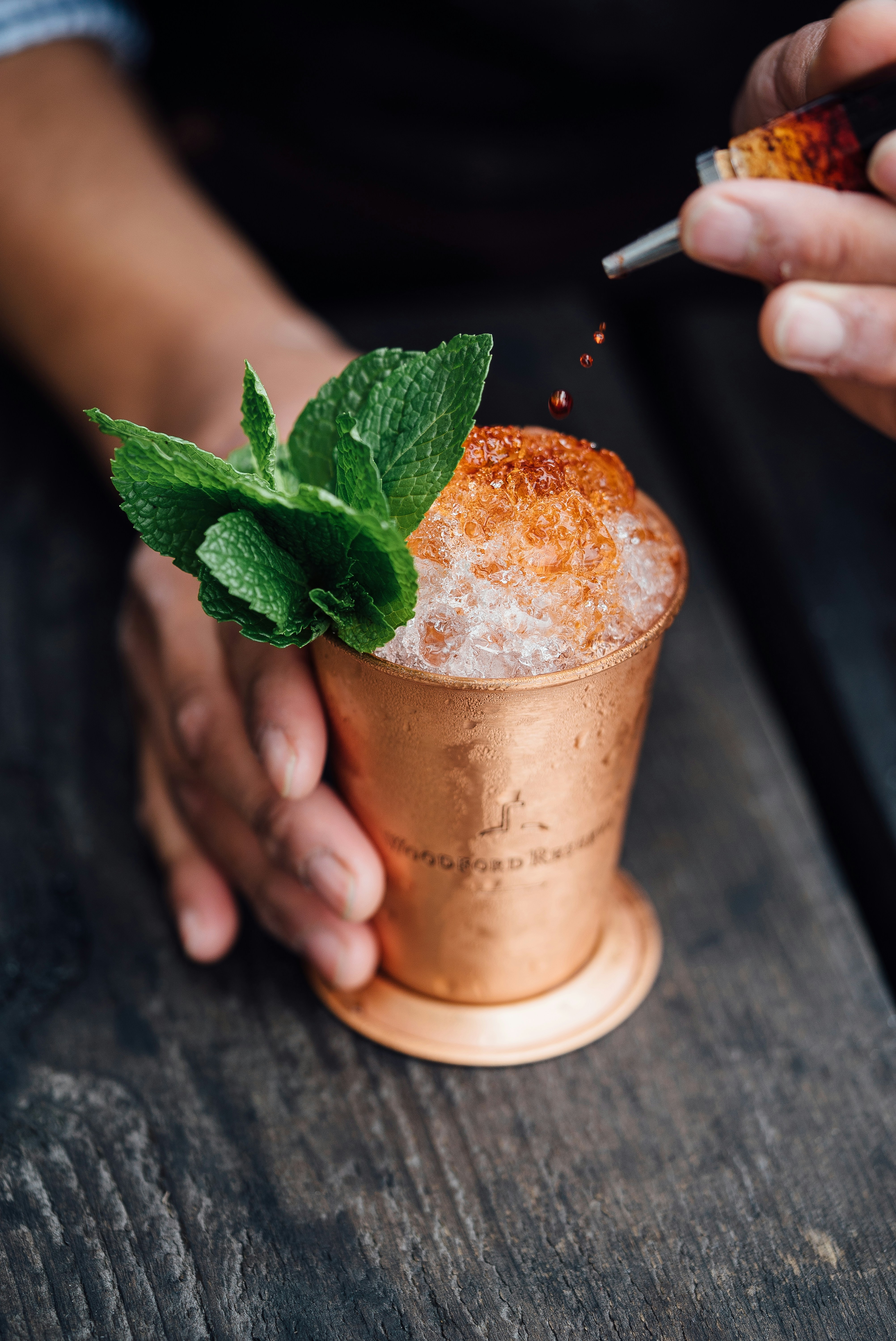 Bitters being dashed into a copper cocktail cup